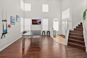 A spacious room with a wooden floor, a dining table, and a staircase with a white railing. - 4BR San Diego Retreat | BBQ & Outdoor Living (San Diego)