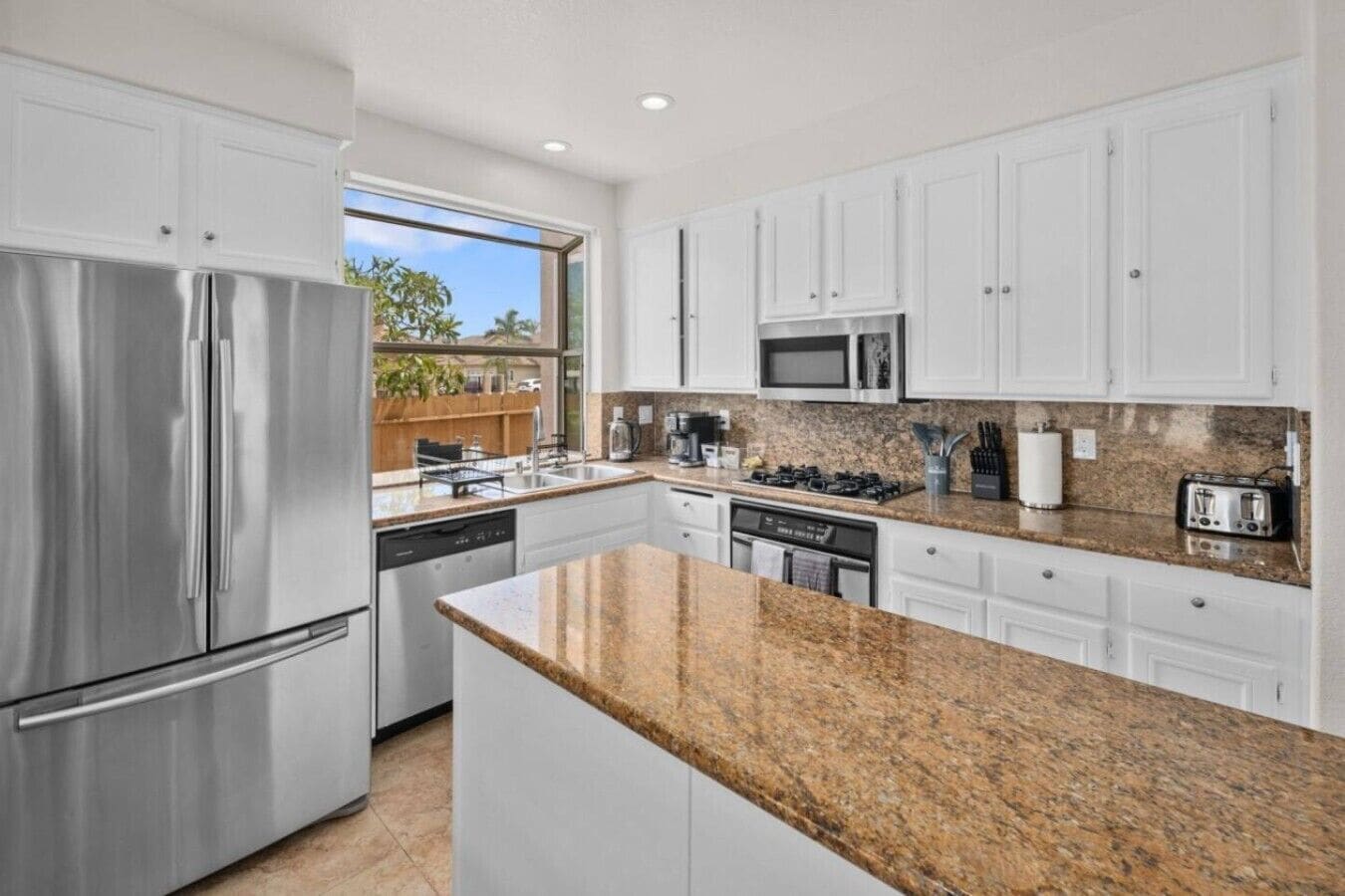 A modern kitchen with stainless steel appliances, granite countertops, and white cabinetry.