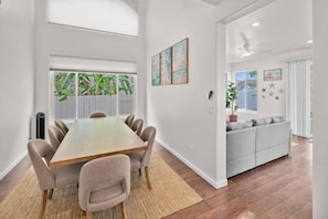 A modern dining area with a wooden table and chairs, a sofa, and a view of greenery outside. - 4BR San Diego Retreat | BBQ & Outdoor Living (San Diego)