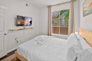 A hotel room with a bed, a television mounted on the wall, a window with curtains, and a view of the outside. - 4BR San Diego Retreat | BBQ & Outdoor Living (San Diego)