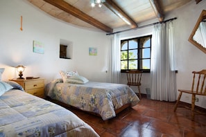 A bedroom with two beds, a window with curtains, a wooden chair, and a nightstand with a lamp. - Traditional Villa With Pool in Pollensa (Pollença)