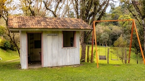 Una pequeña cabaña de madera con un letrero que dice 'CASINHA DA ALINE' en un área con césped y un columpio.