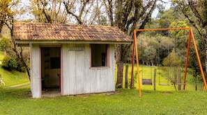 A small wooden cabin with a sign reading 'CASINHA DA ALINE' in a grassy area with a swing set.