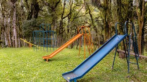 A playground with slides and climbing structures in a grassy area with trees.