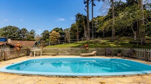 A rectangular swimming pool with a stone border, surrounded by a wooden fence and trees.