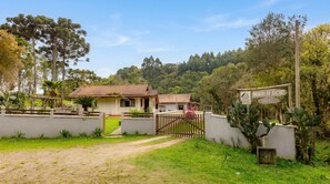A property with a gated entrance, a house with a tiled roof, and a sign indicating the name 'Morro do Bicho'. - Ranch with Pool, Lake and Trail | Jardim da Colina (Campina Grande do Sul)
