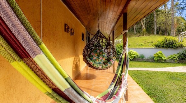 A hammock hanging from a wooden ceiling, a tiled floor, and a garden with grass and plants.
