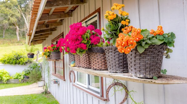 Une série de paniers en osier ornés de fleurs, disposés sur une étagère en bois fixée à un bâtiment.