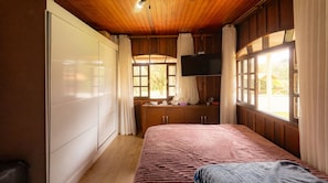 A bedroom with a bed, wooden wardrobe, a television, and windows.