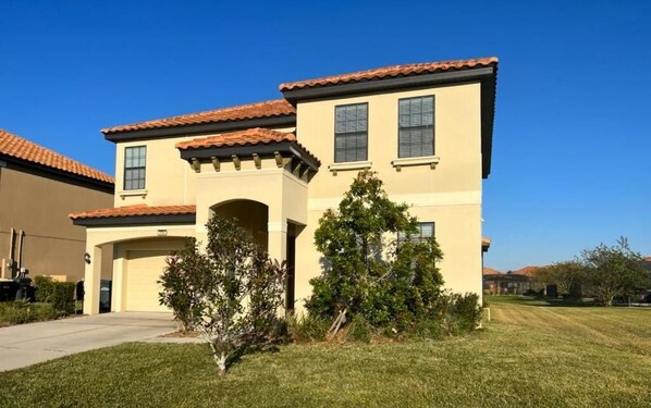 A two-story residential building with a garage, a covered driveway, and a well-maintained lawn. - Rosemont Retreat-5BR Private Pool Home Near Disney with Golf Resort Amenities (Davenport)