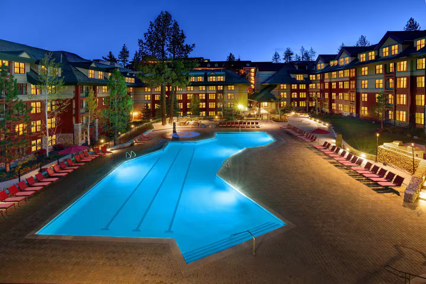 A hotel with a large swimming pool surrounded by lounge chairs and a well-lit building.