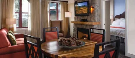 A dining area with a round wooden table, chairs, a fireplace, and a television mounted on a stone wall.