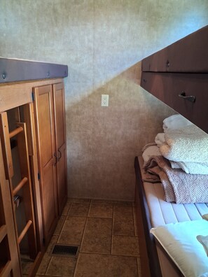 A small, compact room with a wooden wardrobe, a bed with a white mattress and multiple blankets, and a tiled floor. - Marvelous 2-bedroom recreational with AC in Thornville (Thornville)
