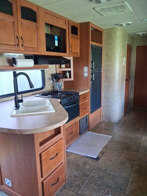 A compact kitchen with wooden cabinets, a gas stove, a black refrigerator, and a built-in microwave. - Marvelous 2-bedroom recreational with AC in Thornville (Thornville)