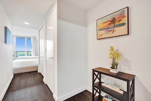 A hotel room with a large window, a bed, a nightstand with a plant, and a painting on the wall. - Lovely Modern Studio - Canal View & Beach Access (Hallandale Beach)