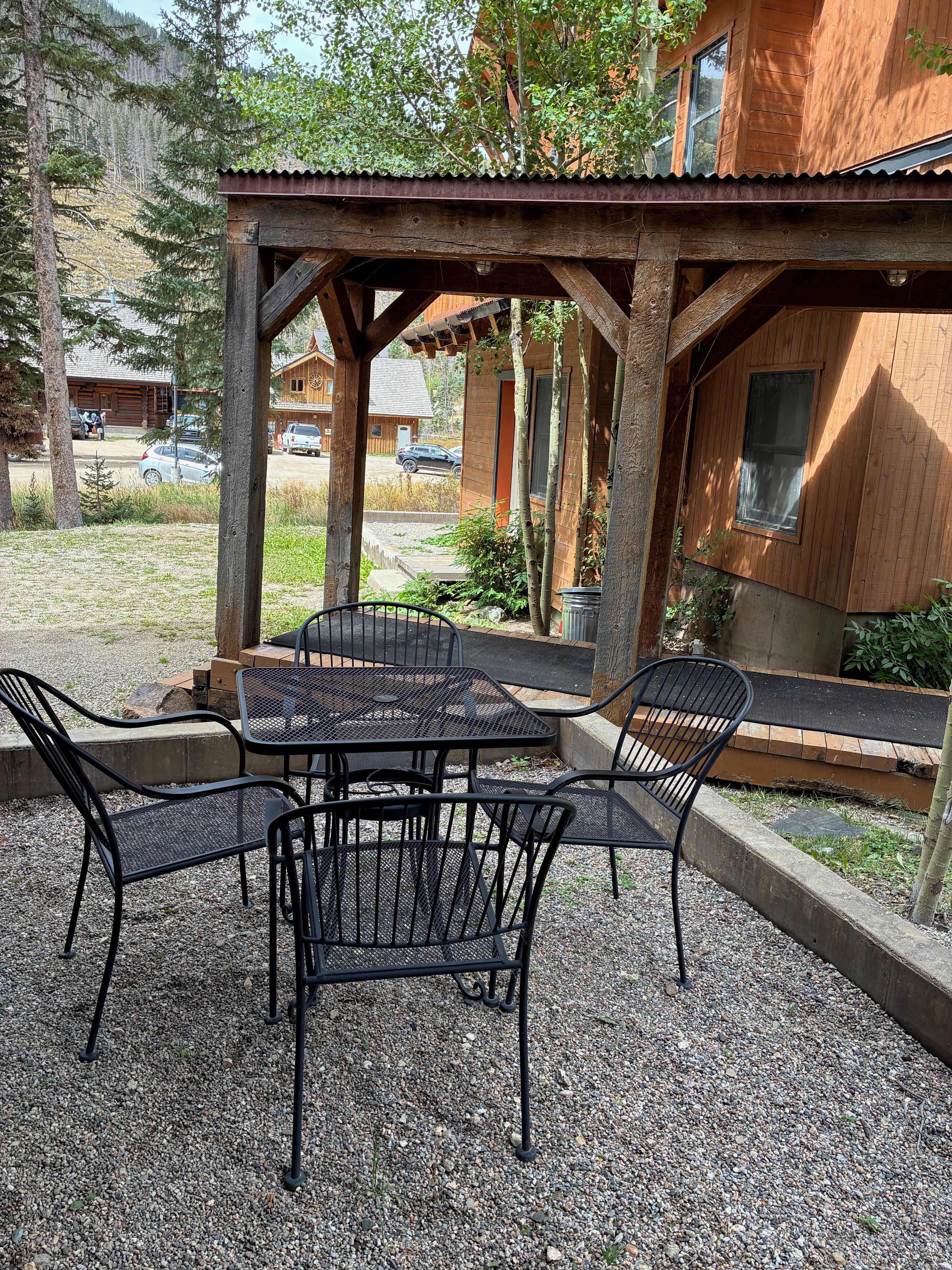 A covered outdoor seating area with a table and chairs, surrounded by gravel and vegetation.