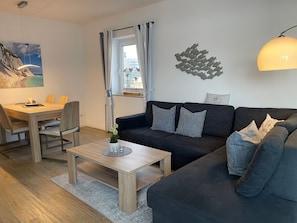 Un salon moderne avec un canapé foncé, une table basse en bois et un coin repas comprenant une table et des chaises.