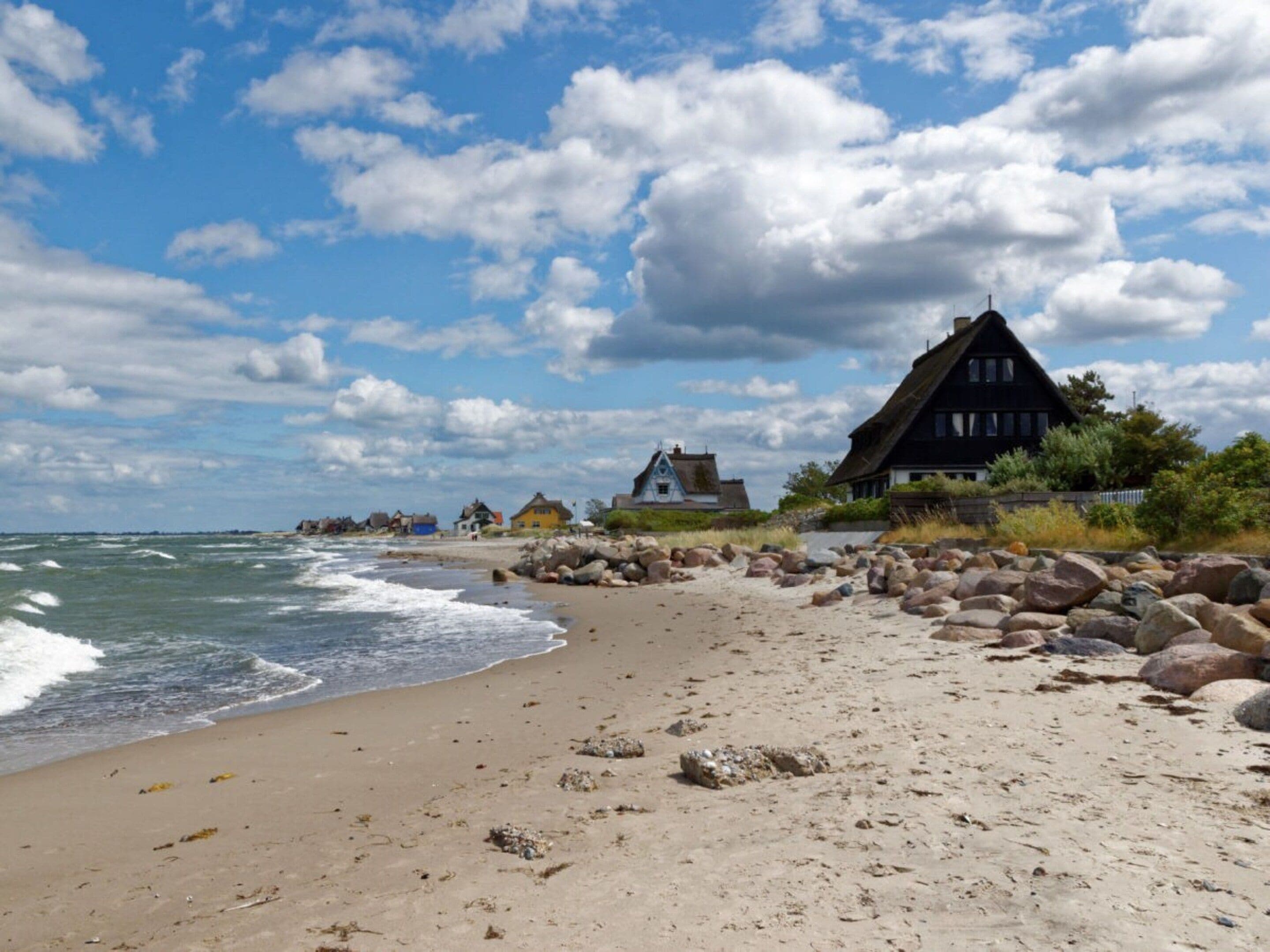 A beach with houses, a rocky shoreline, and the ocean.