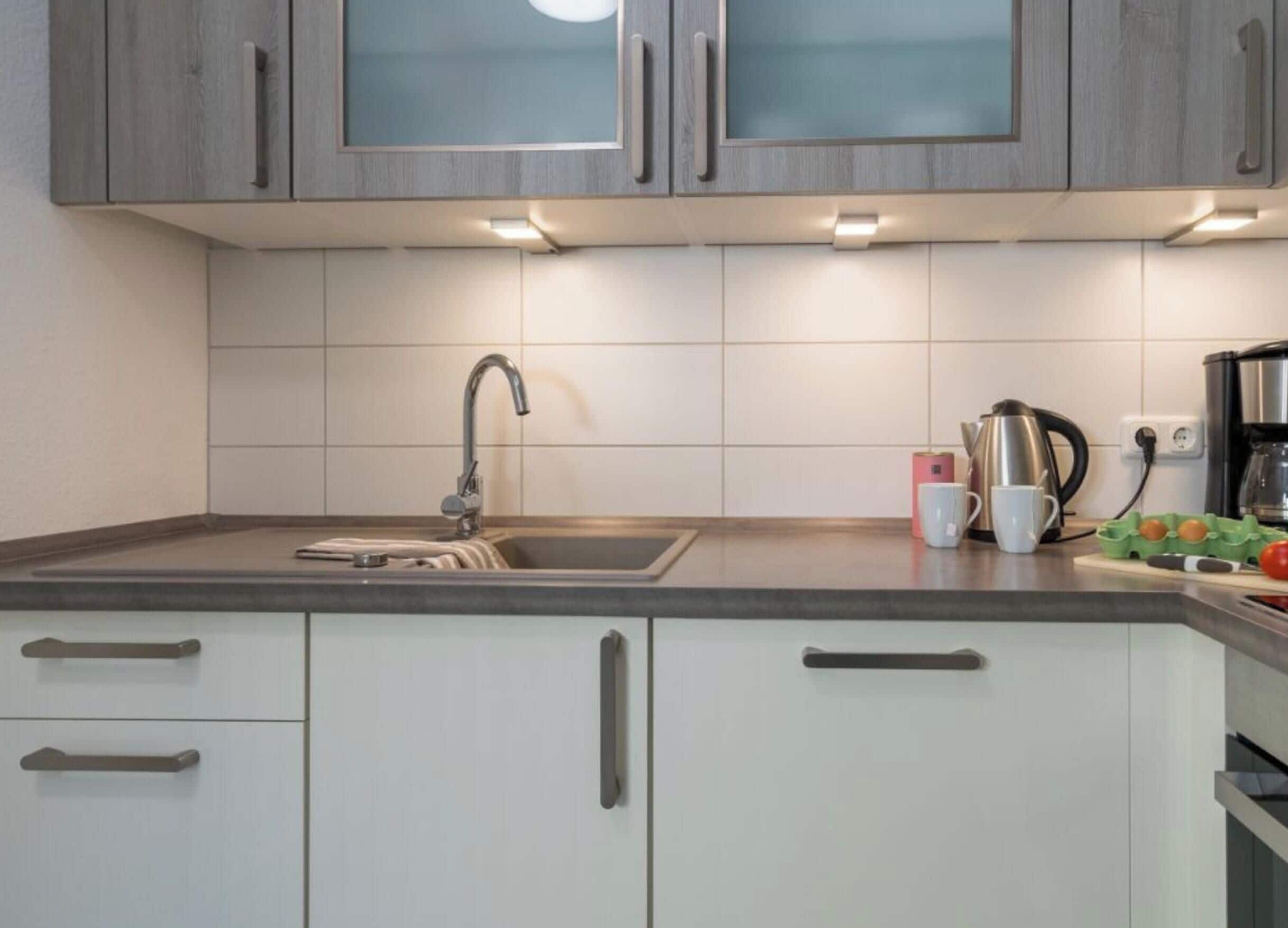 Una cocina moderna con un lavamanos de acero inoxidable, armarios blancos y una encimera con hervidor y cafetera.