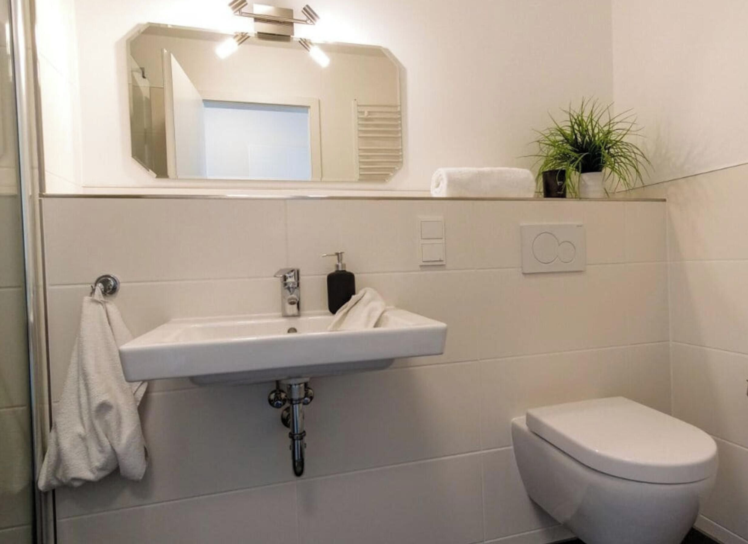Un baño con un lavamanos blanco, un inodoro y un espejo sobre el lavamanos.