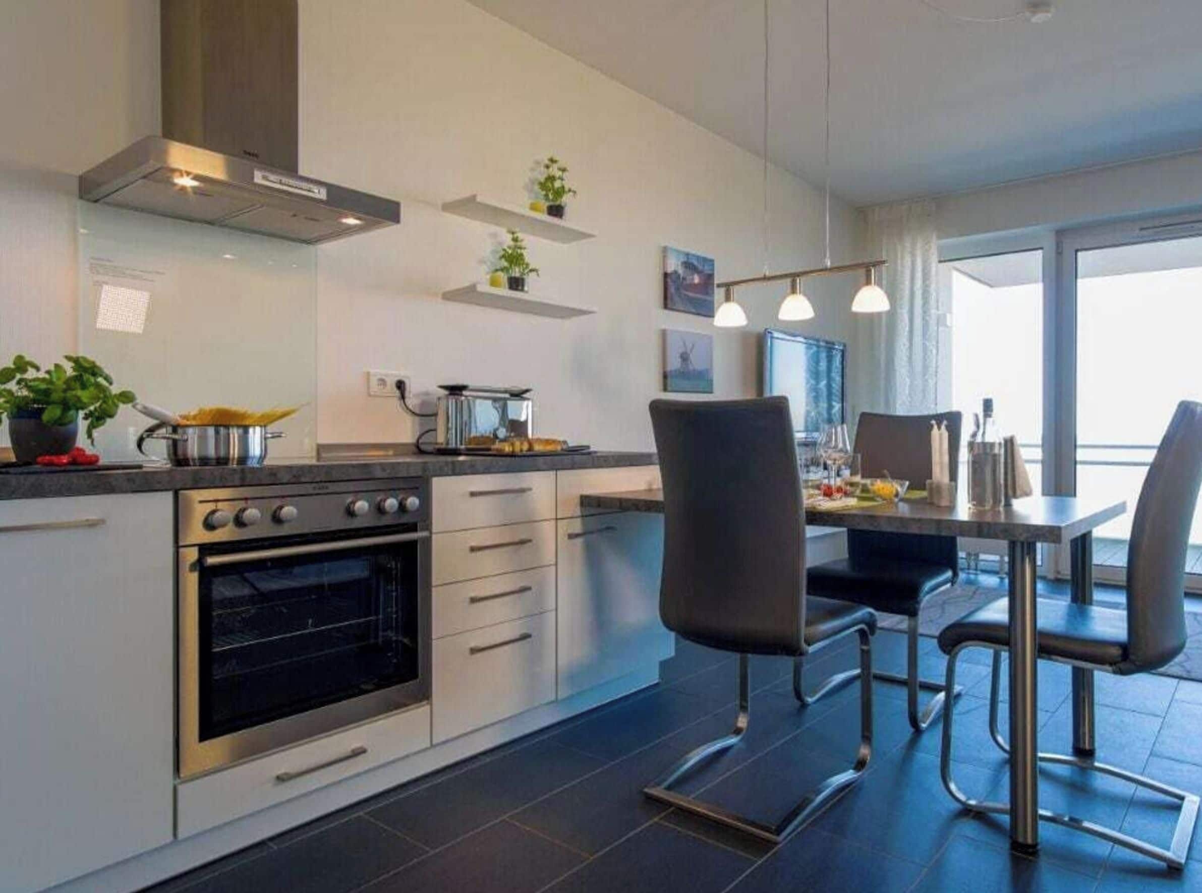 Une cuisine moderne dotée d’un four encastré, un coin repas avec une table et des chaises, et une vue sur l’extérieur grâce à de grandes fenêtres.