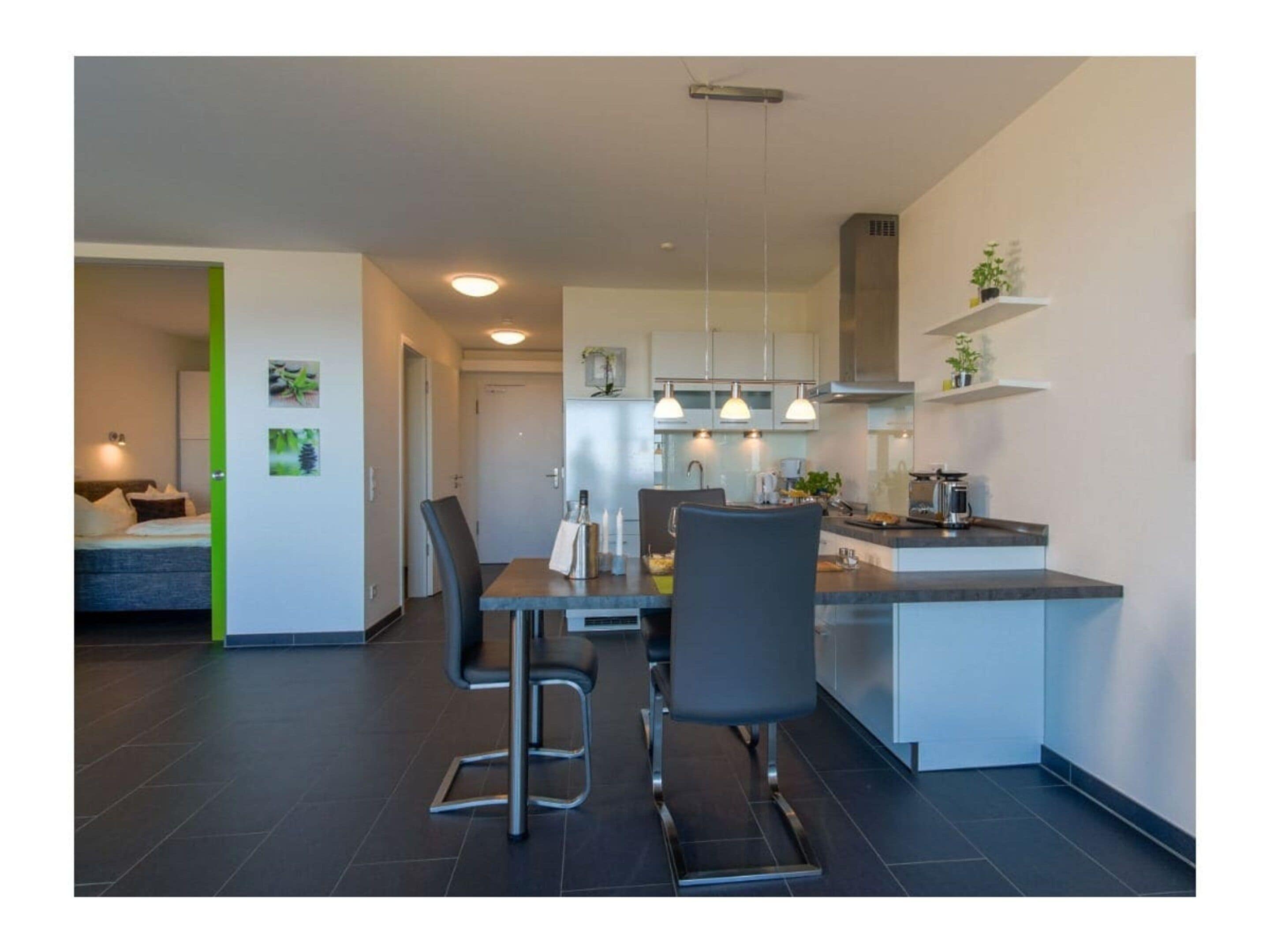A modern kitchen with a dining area, featuring a central island, pendant lights, and a visible stove.