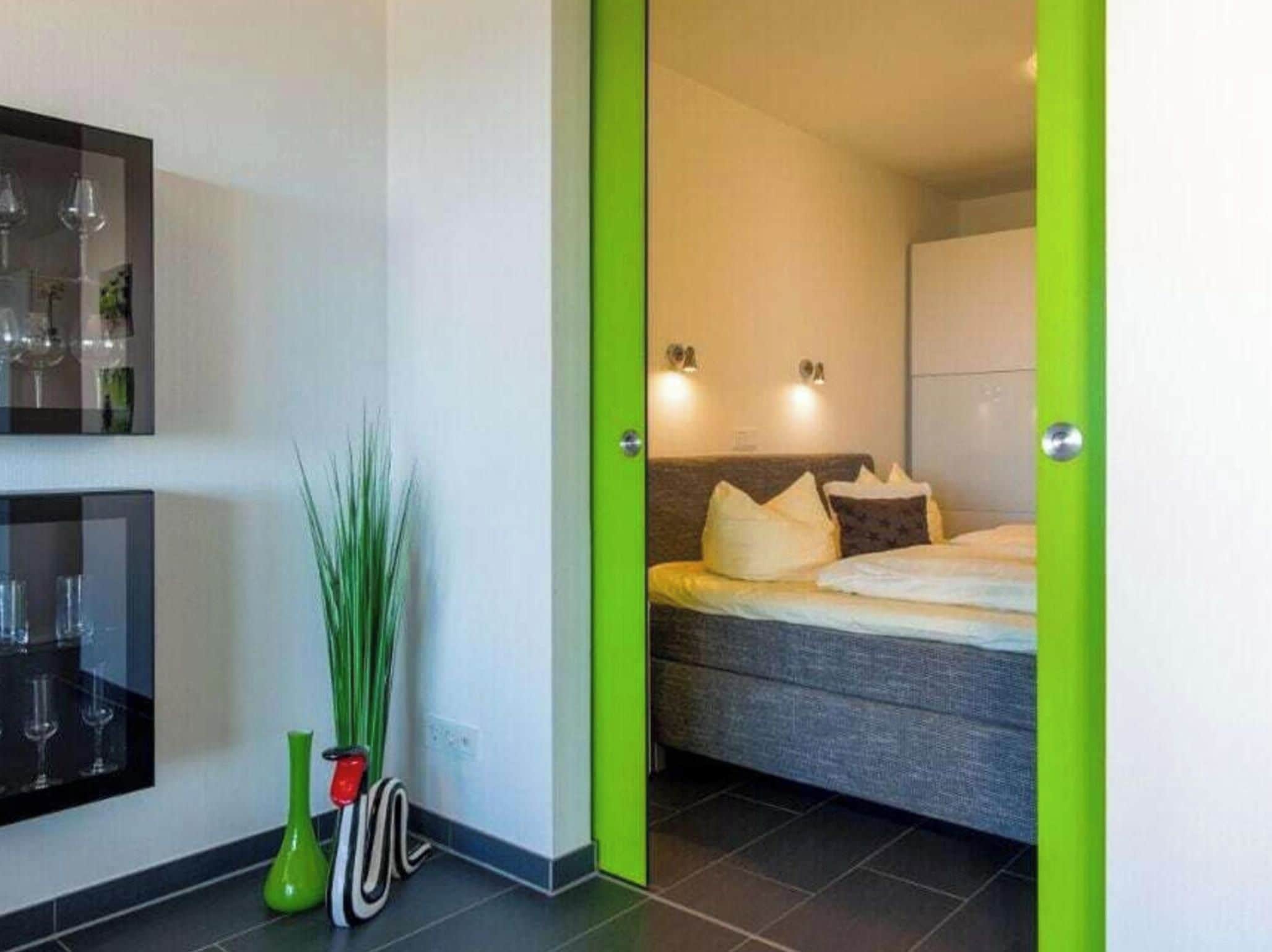 A hotel room with a bed, a nightstand, a mirror, and a green door.
