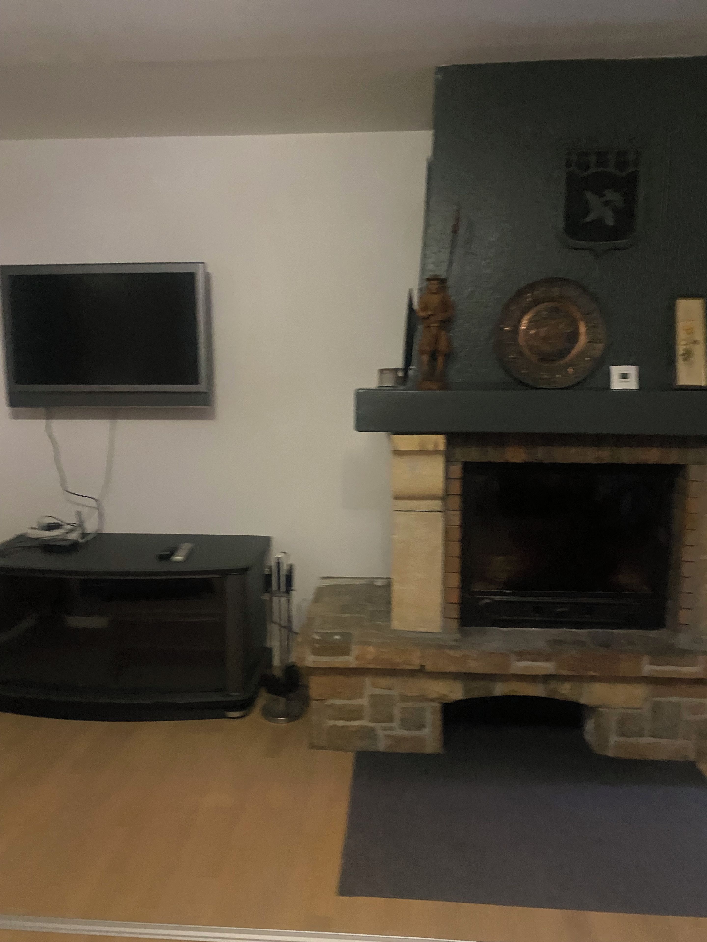 A living room with a stone fireplace, a flat-screen TV mounted on the wall, and a small table with a remote control.