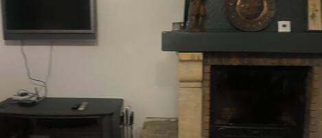A living room with a stone fireplace, a flat-screen TV mounted on the wall, and a small table with a remote control.