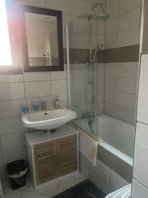 Une salle de bain équipée d’un lavabo, d’un miroir, d’une douche et d’une petite poubelle.