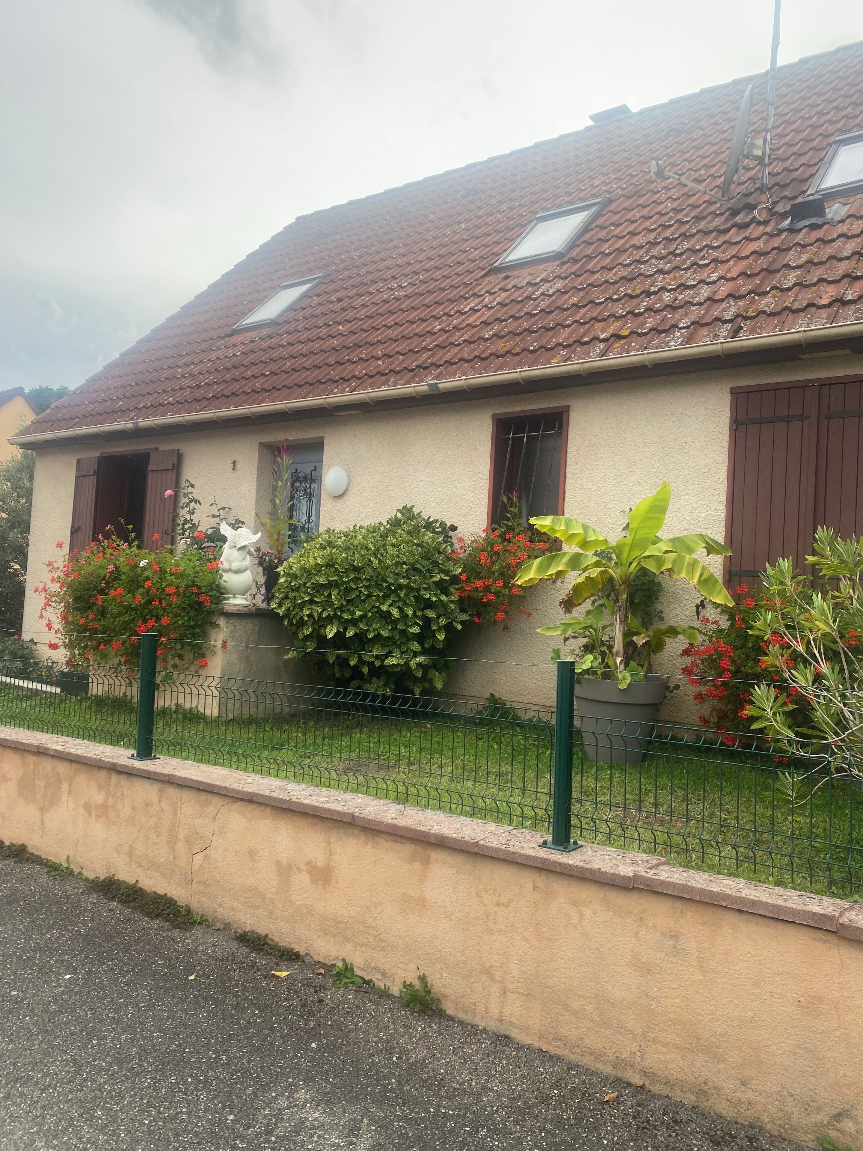 Une maison avec un toit en tuiles, une cour clôturée et diverses plantes.