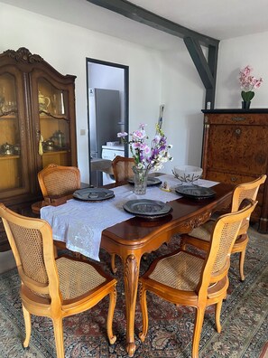 A dining room with a wooden table, four chairs, a vase with flowers, and a cabinet with glassware. - Le Bonheur Vacation Rental (with free parking) (Sundhoffen)