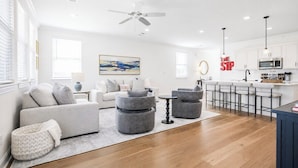 A modern living room with a sofa, ottomans, and a coffee table. There is a kitchen area with a bar and a microwave. - The Summit House, 3BR by Velvet Ditch Villas (Oxford)