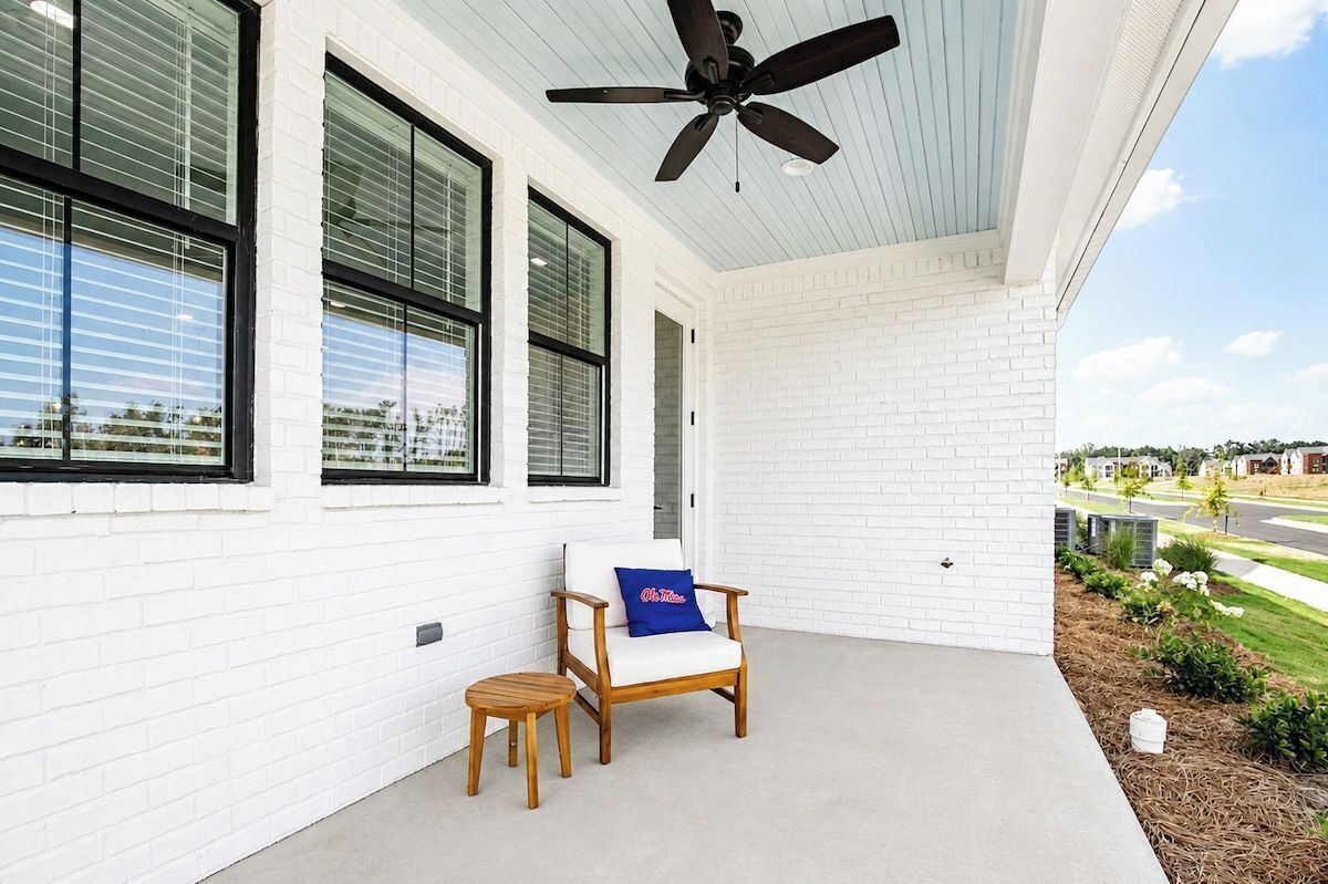 A covered porch with a ceiling fan, a white brick wall, a wooden chair with a cushion, and a small wooden table.