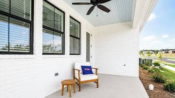 A covered porch with a ceiling fan, a white brick wall, a wooden chair with a cushion, and a small wooden table.