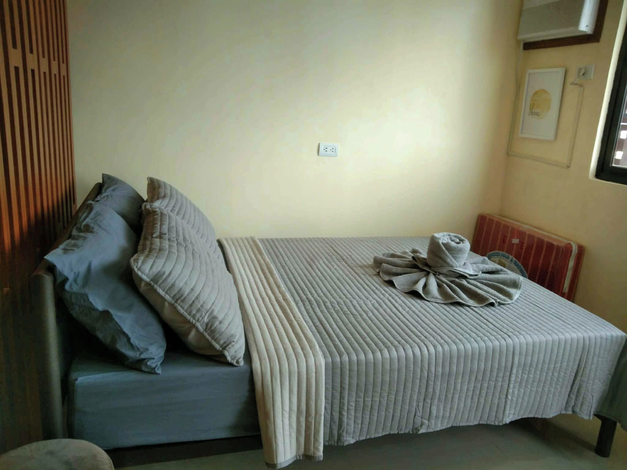 A single bed with a striped bedspread and pillows, a power outlet on the wall, and a radiator on the right.