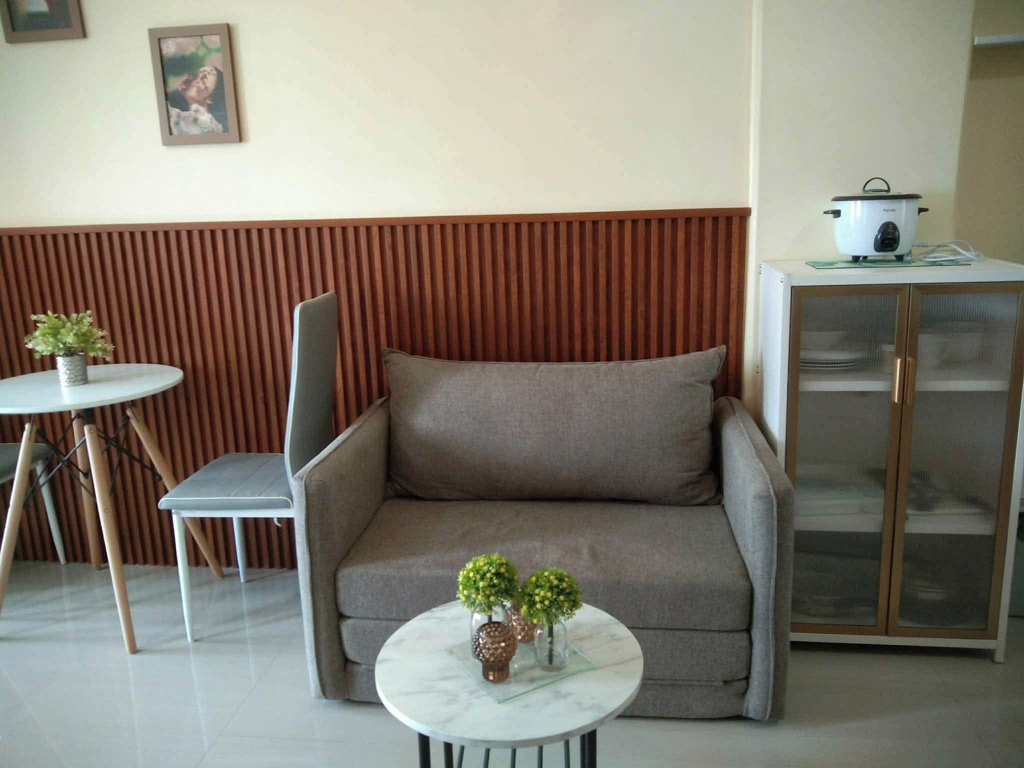 Uma sala de estar com sofá, mesa de jantar com cadeiras, uma pequena planta em vaso e um armário com um vaso em cima.