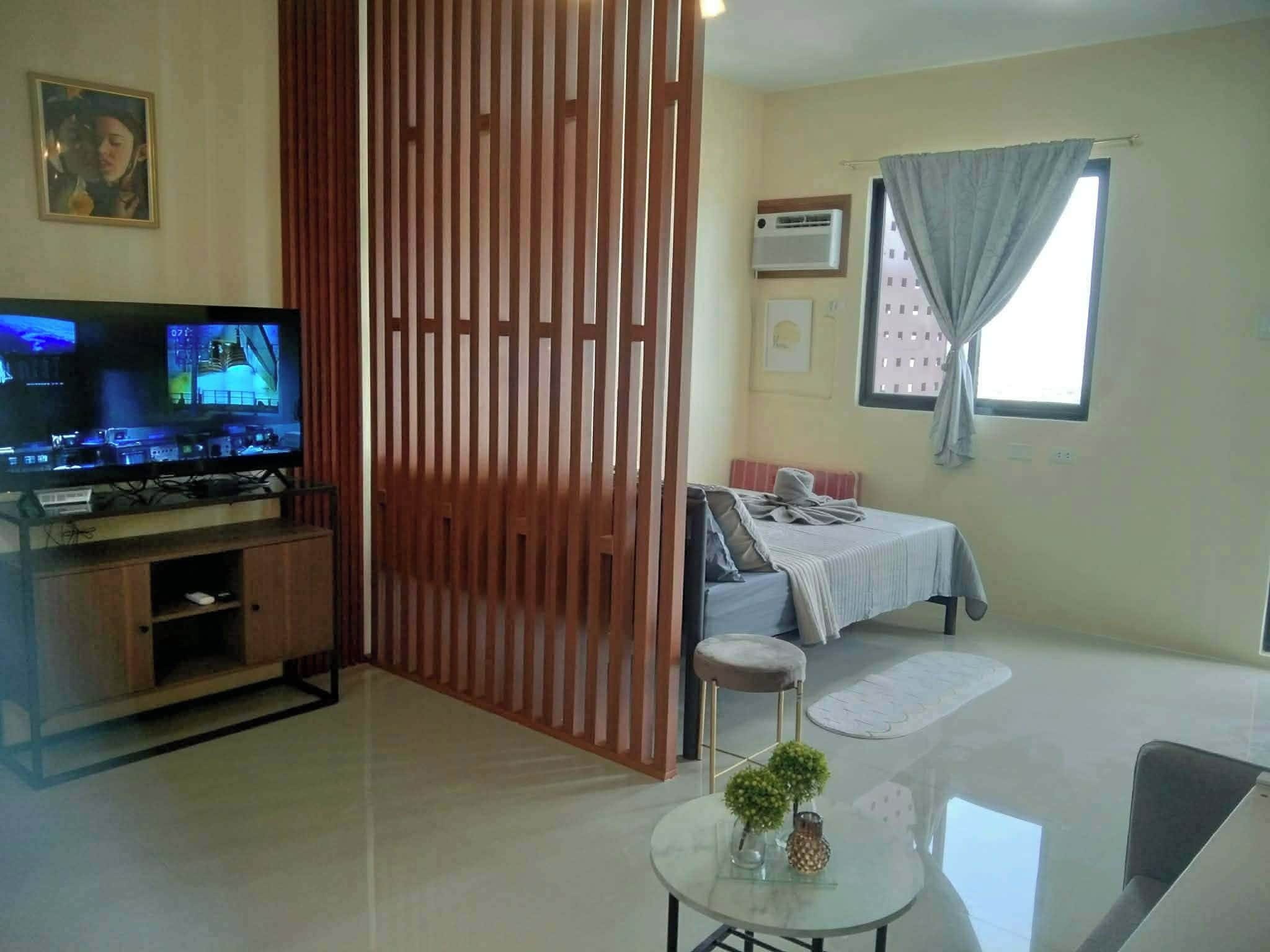 A living room with a television, a sofa, a coffee table, and a window with curtains.