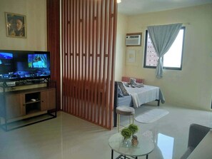 A living room with a television, a sofa, a coffee table, and a window with curtains. - Royal Oceancrest Mactan 1BR (Lapu-Lapu)