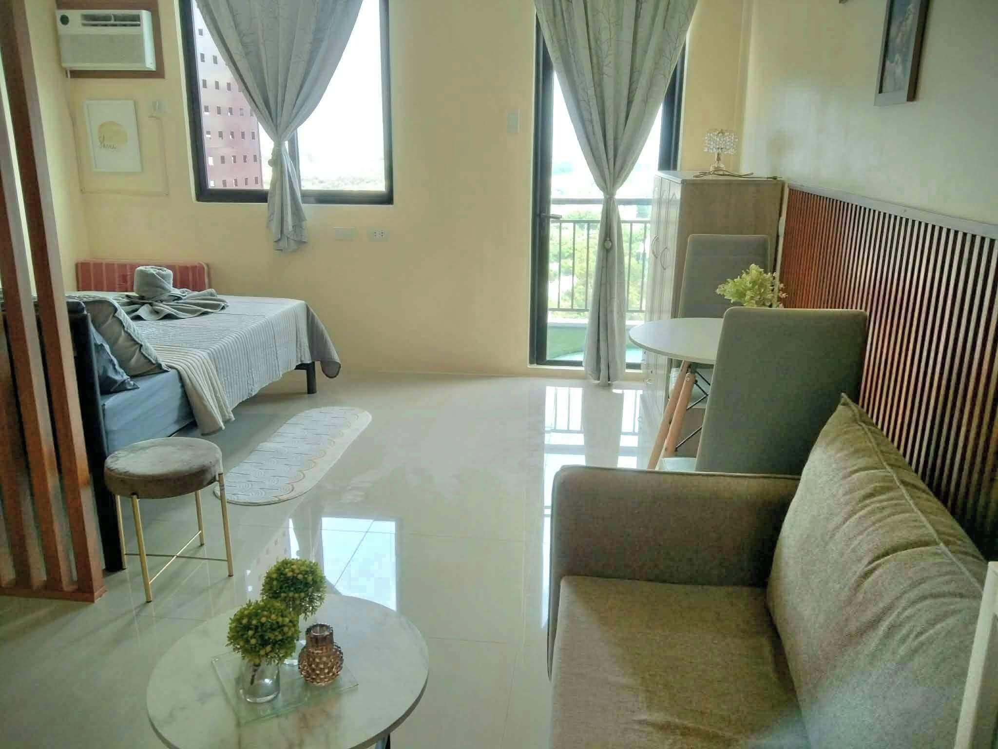 Ein Hotelzimmer mit Bett, einer Sitzecke, einem kleinen Tisch mit Blumenvase und einem Balkon mit Vorhängen.
