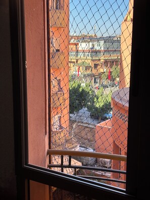 A view through a window with a chain-link fence, featuring a building with multiple balconies and a clear sky. - Apartment in the heart of Gueliz (Marrakech)