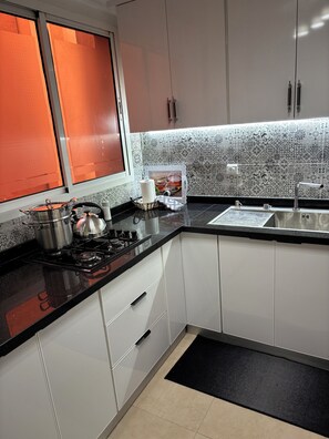 A modern kitchen with a gas stove, stainless steel pots, a black countertop, white cabinets, and patterned backsplash. - Apartment in the heart of Gueliz (Marrakech)