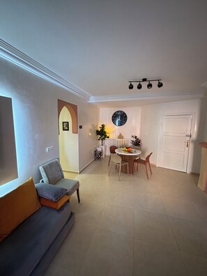 A living room with a sofa, a dining table with chairs, a clock on the wall, and a door. - Apartment in the heart of Gueliz (Marrakech)