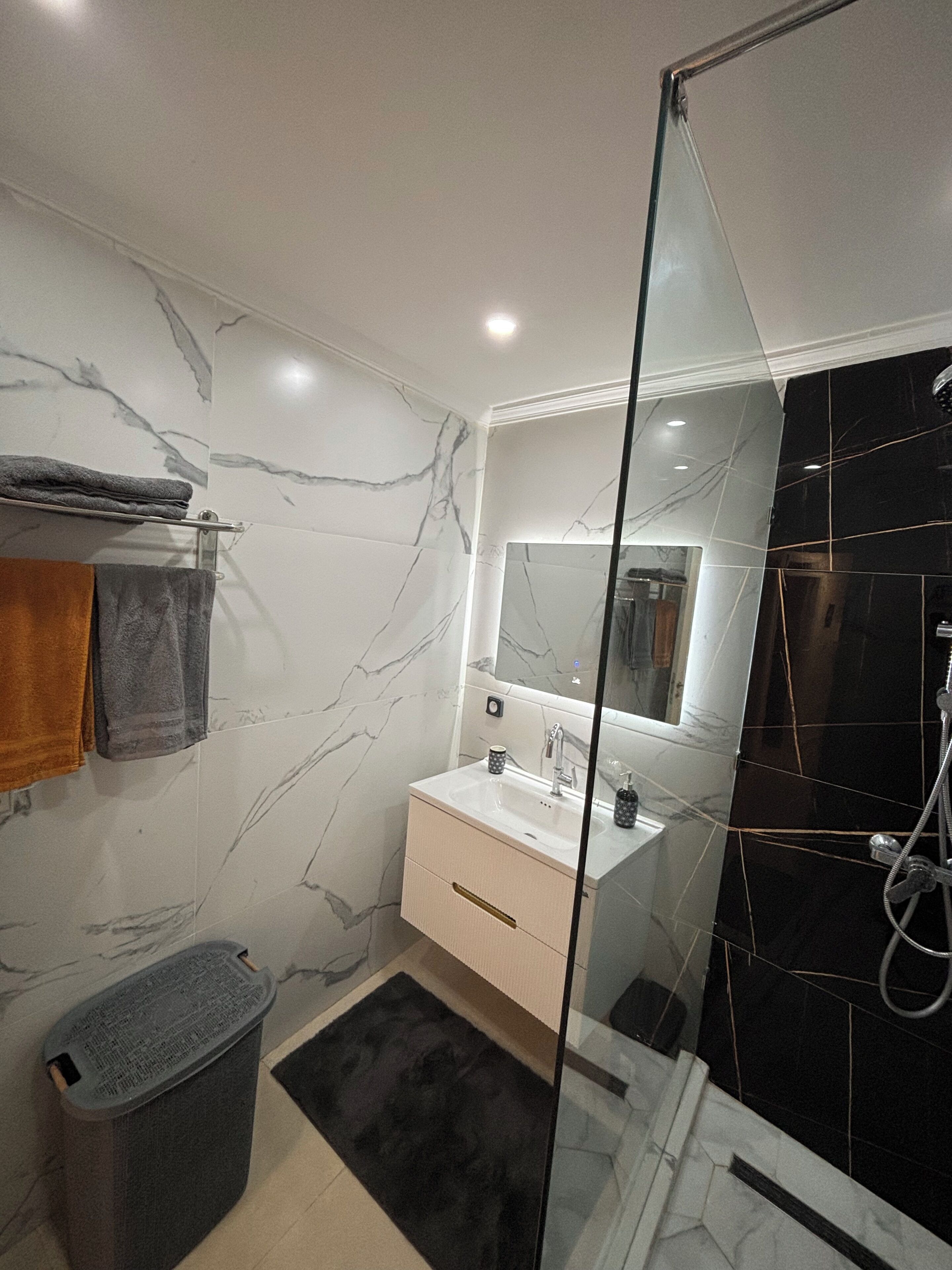 A modern bathroom with a glass shower enclosure, a white sink with a marble countertop, and a large mirror above the vanity.