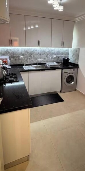 Cozinha compacta com fogão a gás, pia e máquina de lavar roupa.