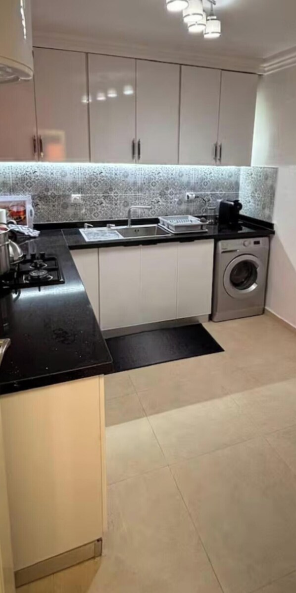 A compact kitchen with a gas stove, a sink, and a washing machine. - Apartment in the heart of Gueliz (Marrakech)