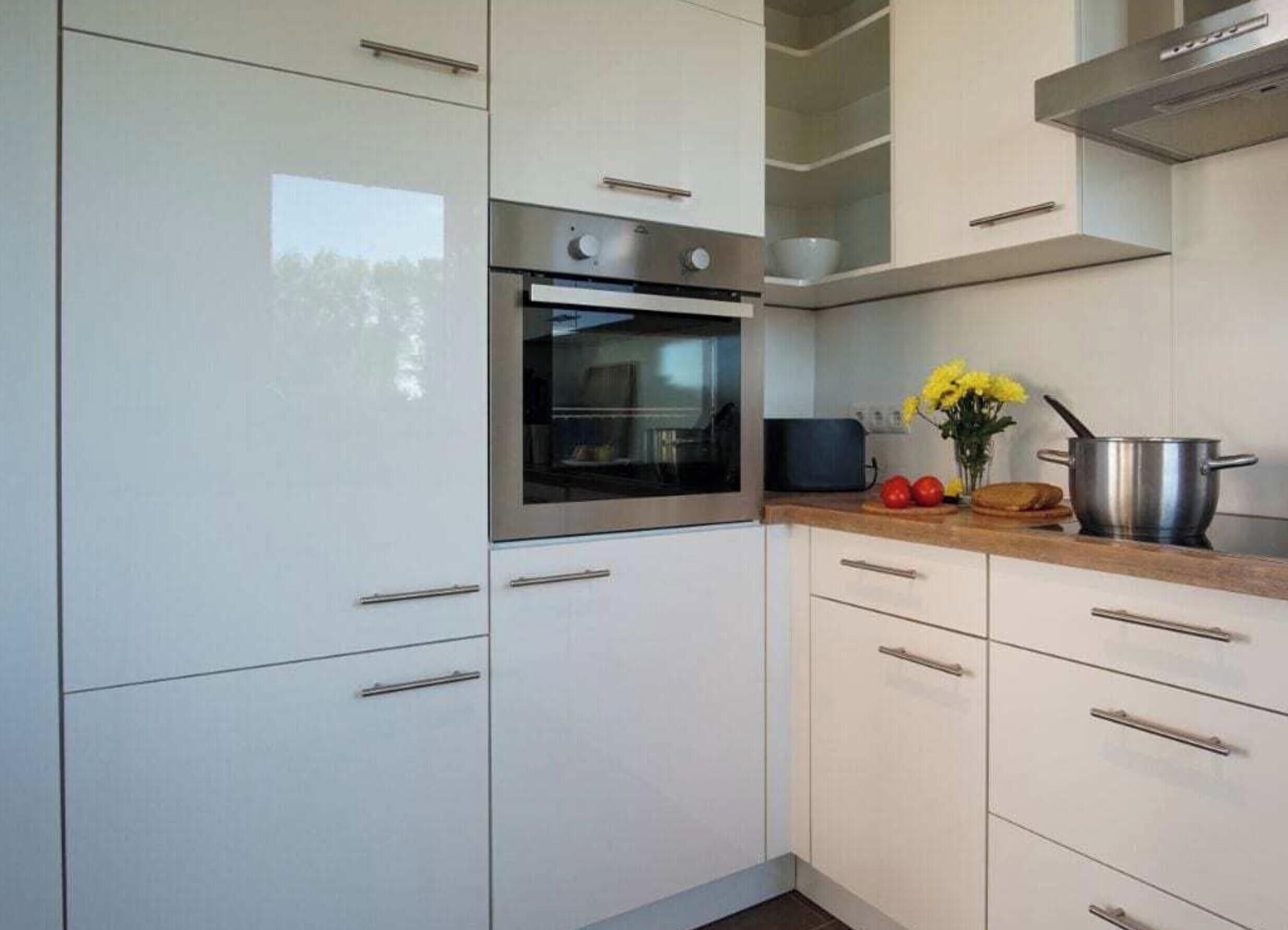 A kitchen with white cabinets, a stainless steel oven, and a countertop with a pot and vegetables.