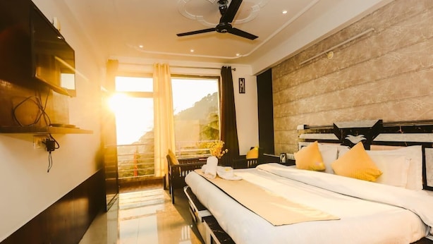 Ein Hotelzimmer mit Bett, Deckenventilator, Fenster mit Vorhängen und Blick ins Freie.