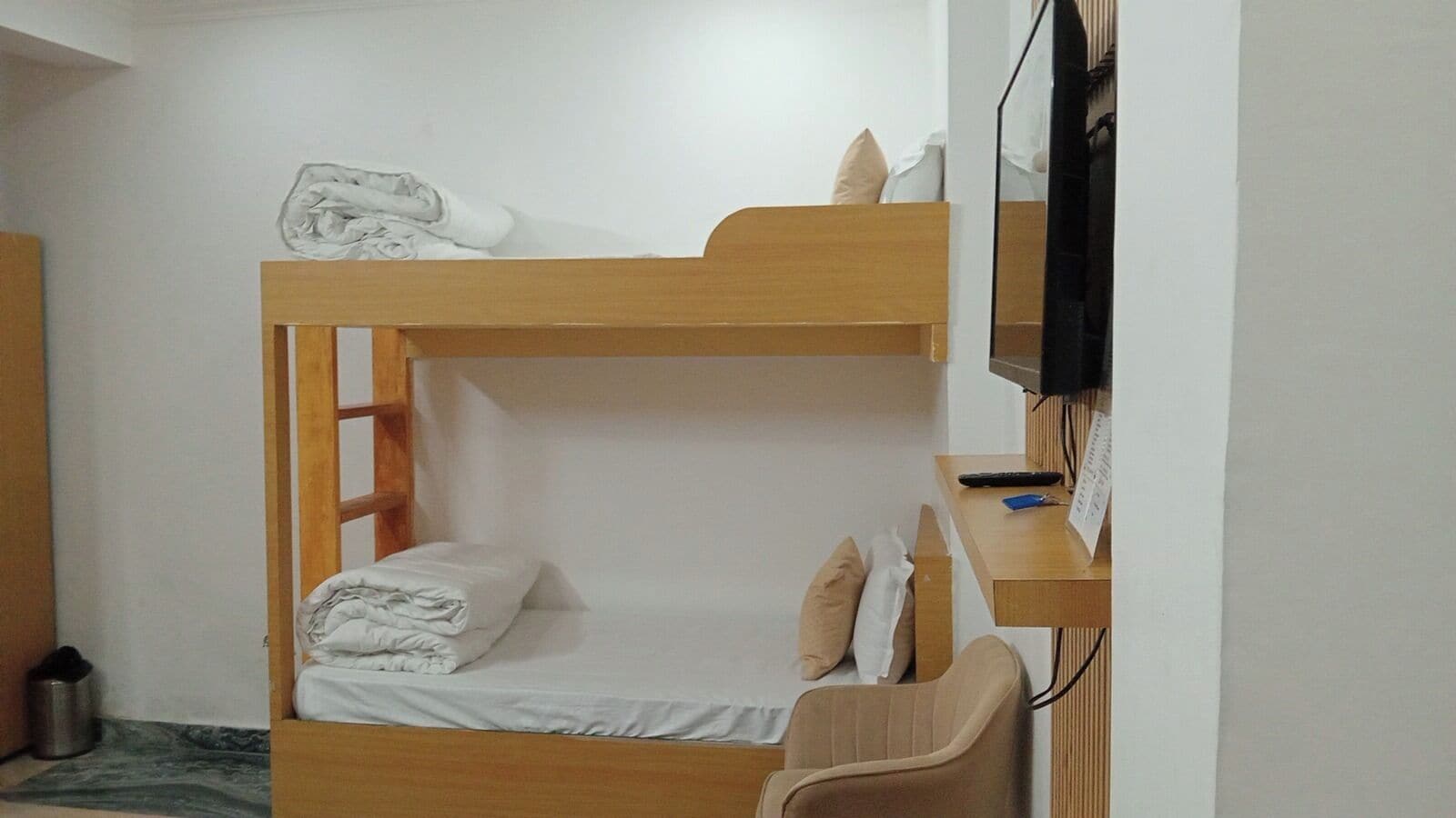 A bunk bed with a desk and chair, a television, and a small trash can.