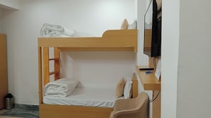 Una cama litera con escritorio y silla, un televisor y un cesto de basura pequeño.